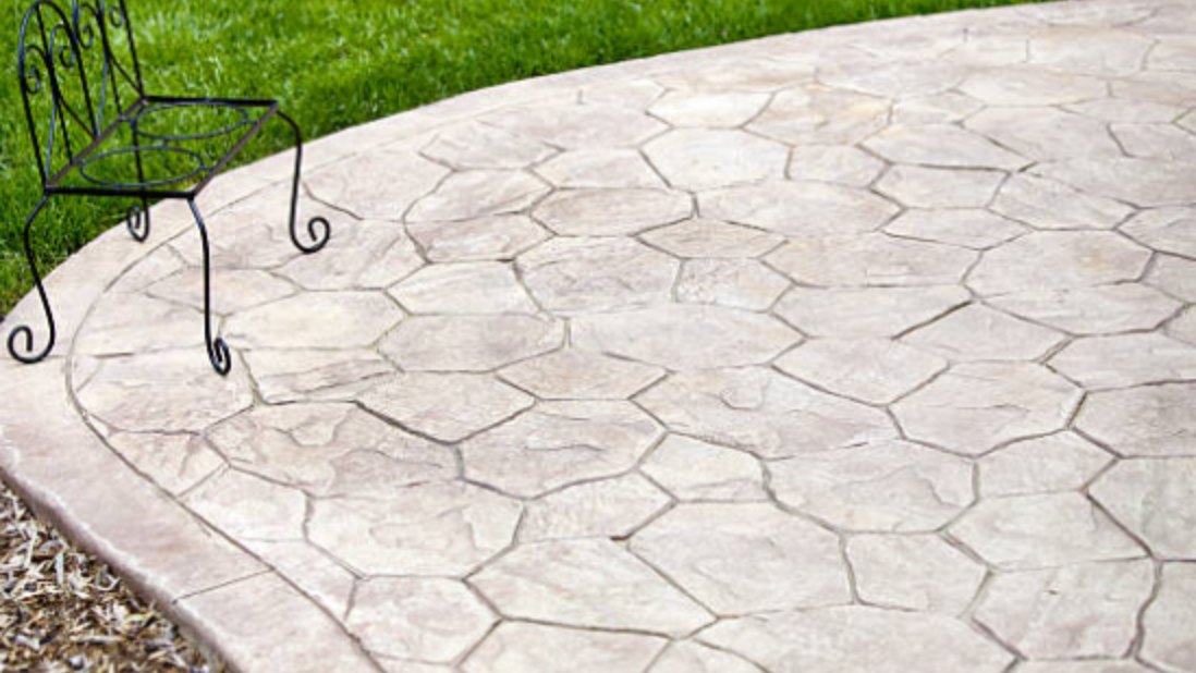 Stamped concrete patio in a random flagstone pattern, curving into a lawn with a metal chair on it