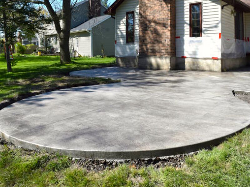 Curved concrete patio with saw-cut joints poured against an older brick home