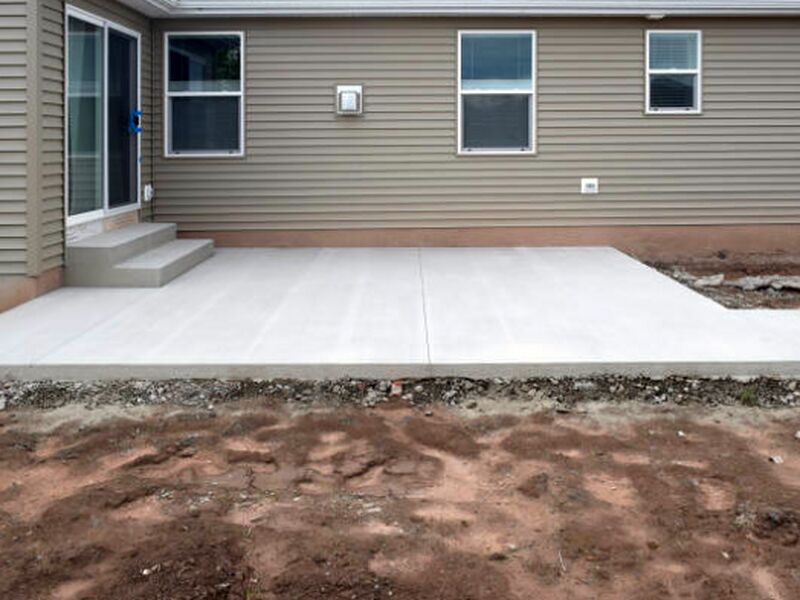 New concrete patio slab and poured steps with bare graded soil around the edges